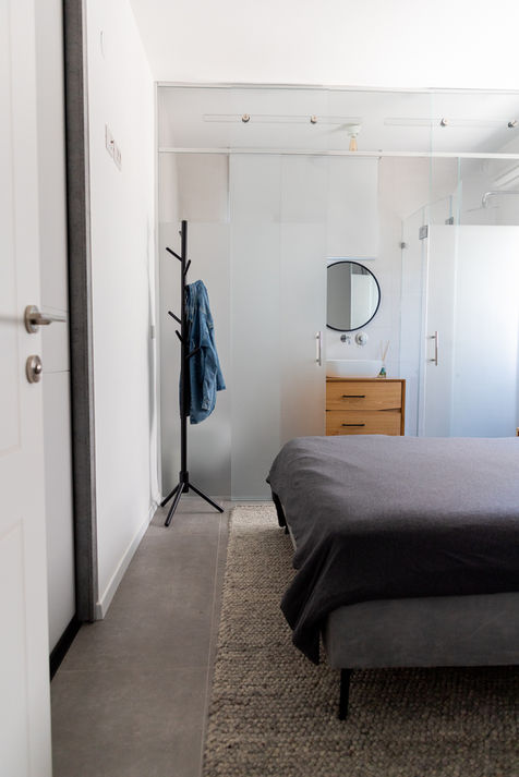 חדר שינה עם מיטה אפורה ושירותים ברקע