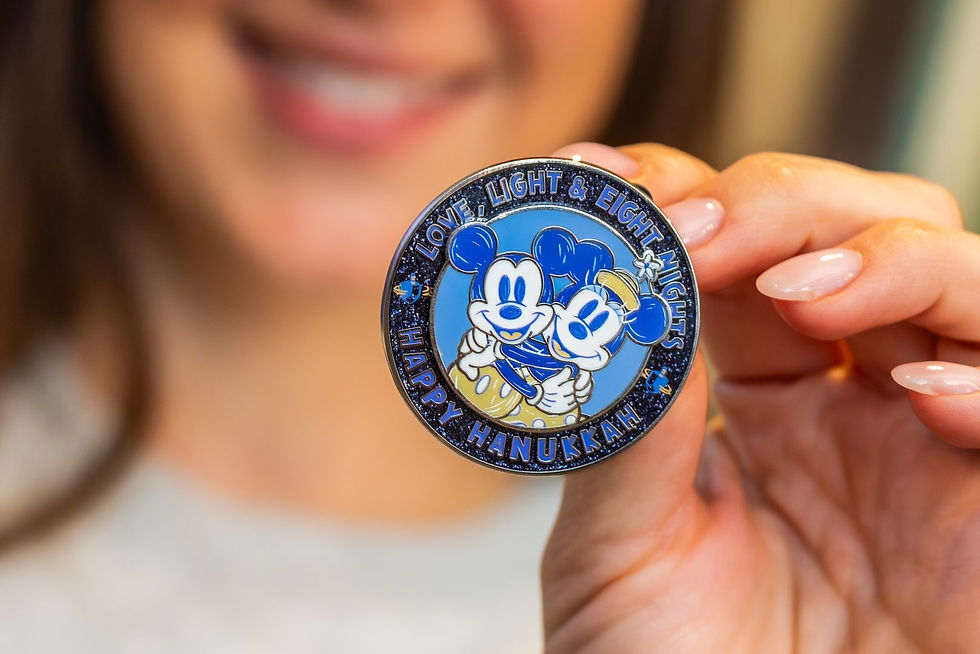 A person holds a blue and silver coin featuring two cartoon characters, surrounded by text "Love, Light & Eight Nights. Happy Hanukkah."