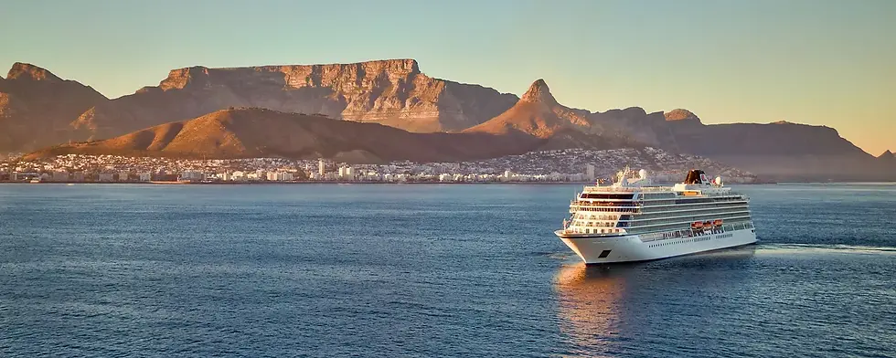 Cruise ship sails near a coast with mountains in the background under a clear sky. The sun casts a warm glow over the landscape and water.