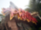 Red "River Adventure" sign on a rocky structure, surrounded by palm trees, under a bright sky. The scene feels tropical and adventurous.