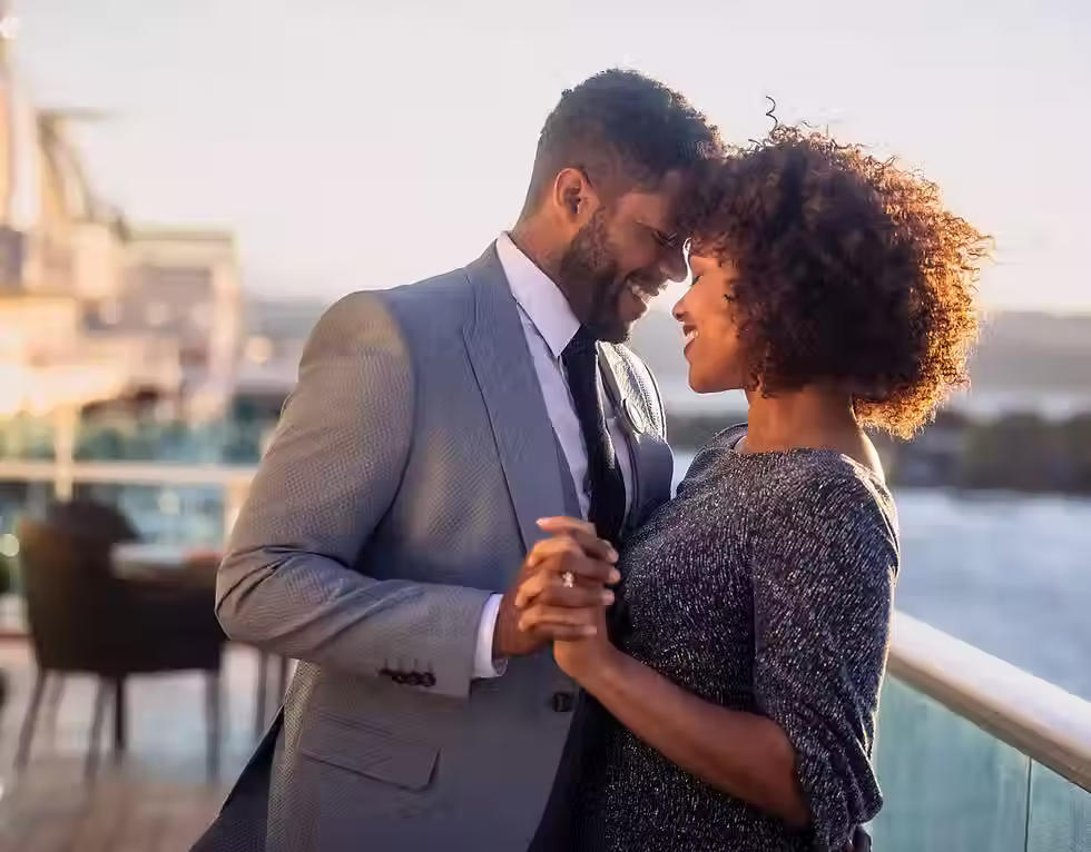 A couple is smiling, holding hands on a deck of a cruise ship.