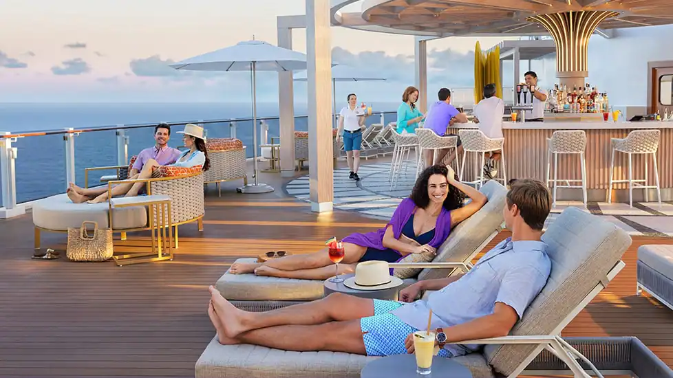 People enjoying a cruise deck on lounge chairs and sitting at a bar. A bartender is serving a drink.