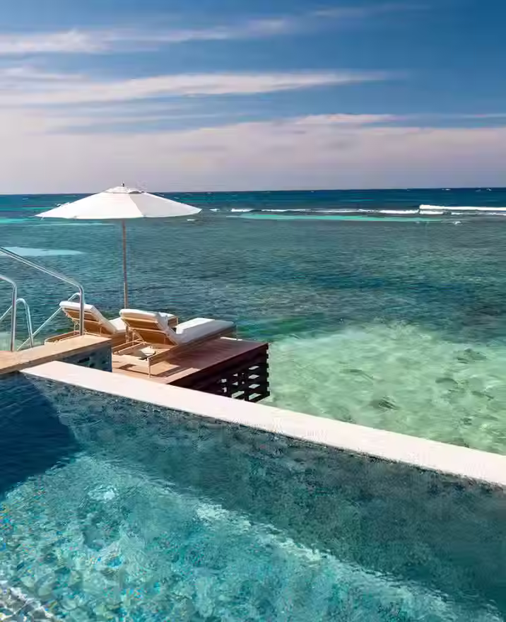 An infinity pool overlooking the ocean. There are two chairs and an umbrella in the background.
