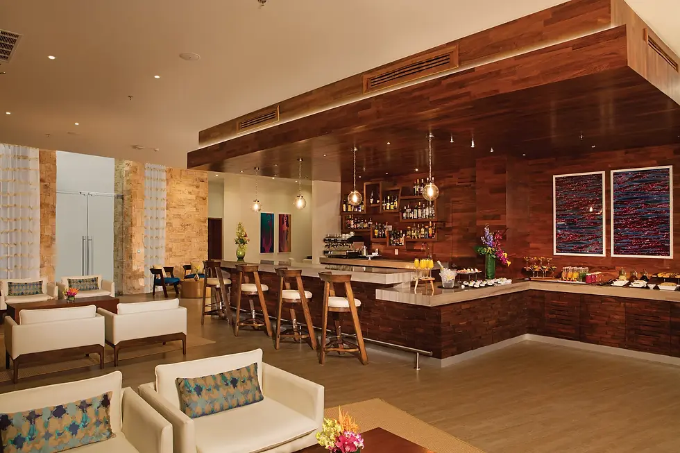 Empty upscale lounge bar with wood-paneled counter, tall stools, pendant lights, white sofas, and colorful wall art.