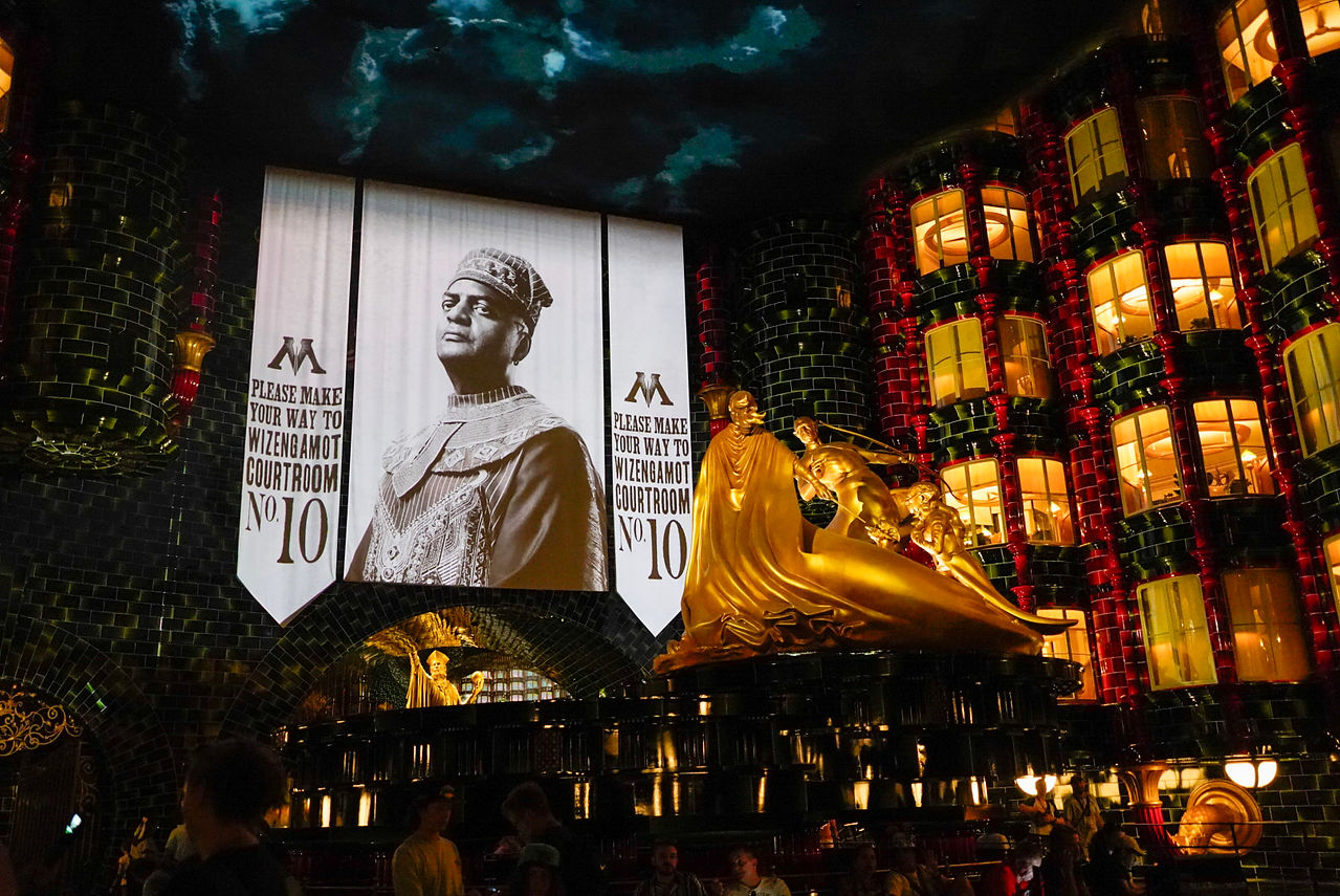 Banners with a wizard pointing at the camera is in the background. The ceiling looks like a storm. A gold statue sits in the center.