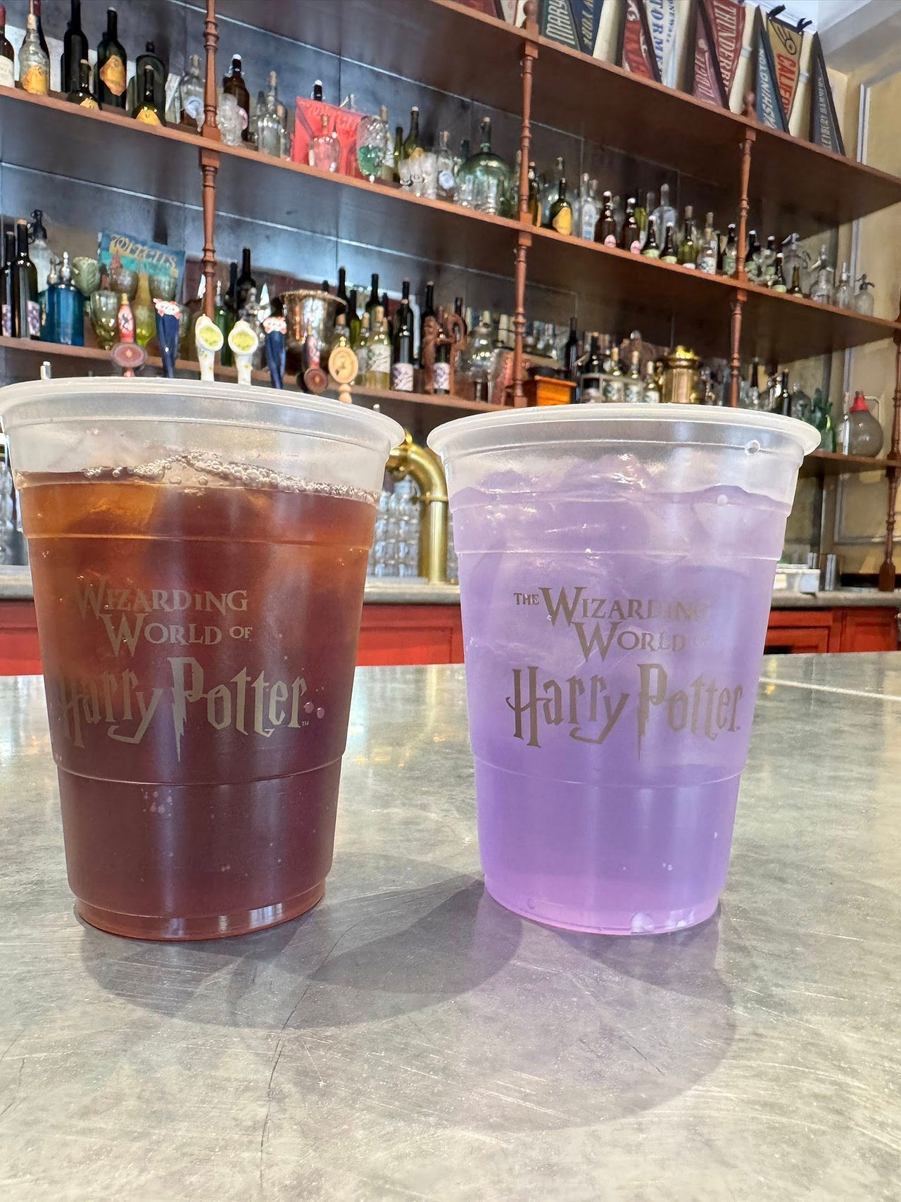 Two drinks, one brown, one purple with the logo "The Wizarding World of Harry Potter." There is a bar in the background.