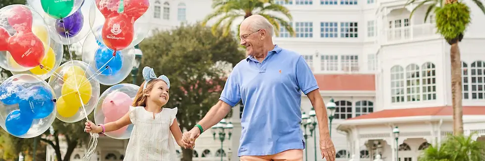 Older man and young girl holding hands and colorful Mickey balloons outside a Disney resort, smiling happily