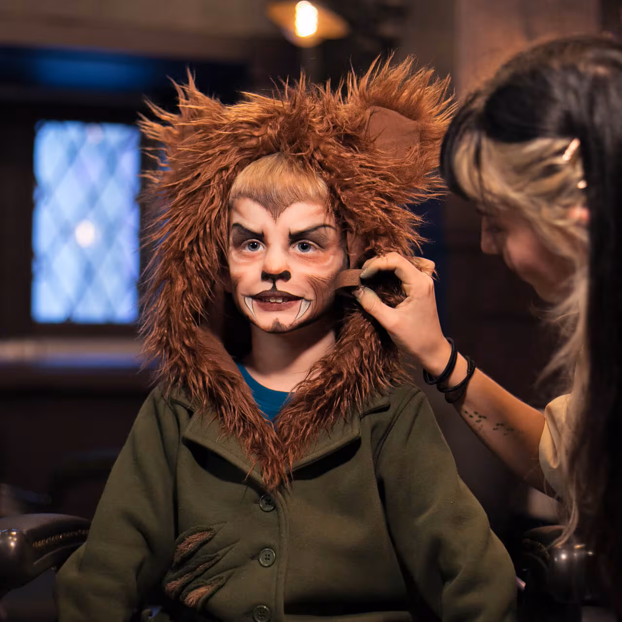 A child getting makeup placed on their face is dressed like a werewolf.