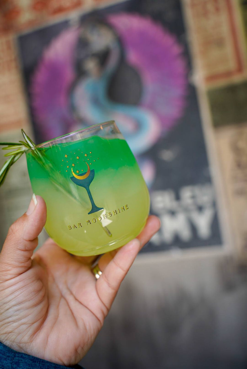 A green and yellow drink in a cup with the logo Bar Moonshine. A blue and purple dragon is in the background.