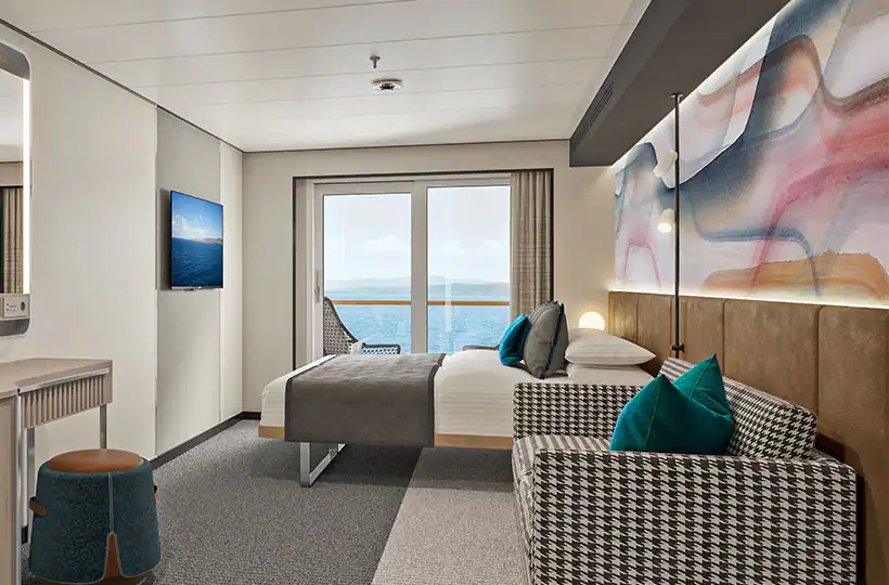 A room with a bed, couch, mirror, and TV. The room is decorated in black, white, and teal. There is a view of the ocean.