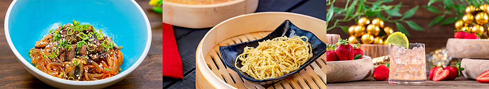 A blue bowl of beef noodles, steamed noodles in a bamboo tray, and a cocktail with strawberries and lime on a wooden table. Vibrant colors.
