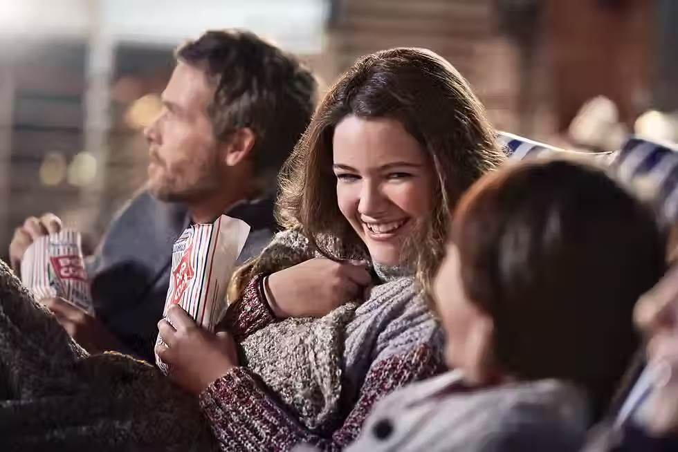 A family is watching a movie. They are bundled up and eating popcorn.