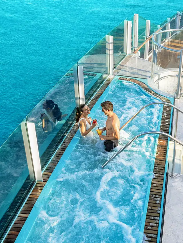 A couple are enjoying a hot tub on a deck of a cruise ship. The ocean is in view as well.