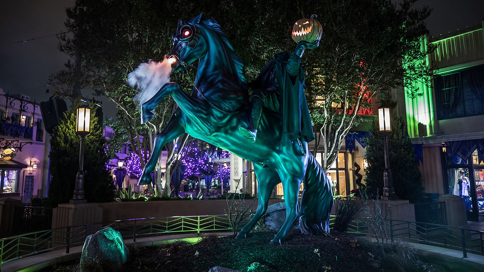 Glowing teal horse statue rears at night with pumpkin-headed rider in a Halloween-lit plaza.