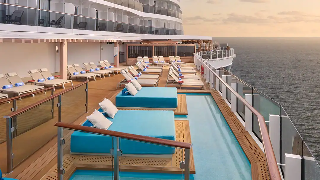 Teal lounge beds surrounded by a hot tub on a cruies ship deck at sunset.