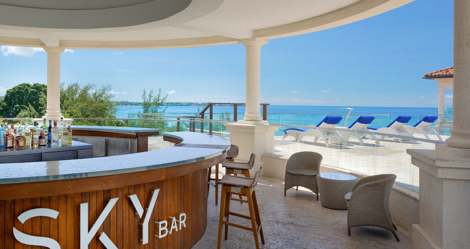 A rooftop bar named "Sky Bar" overlooks the ocean. There is bar seating and beach style lounge chairs.
