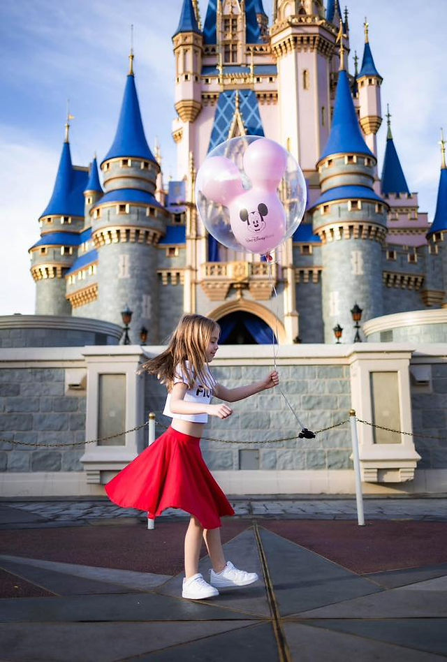 A little girl holding a ballon, jumps in front of Cinderella Castle at Disney World