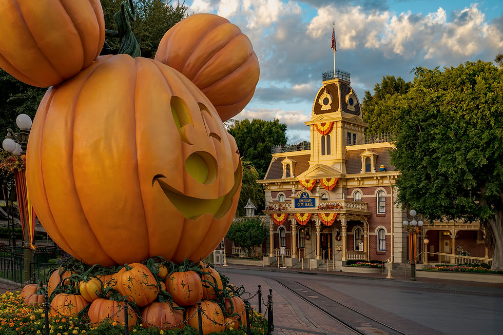 Giant Mickey-shaped pumpkin display beside Disneyland City Hall, decorated with orange bunting under a cloudy sky.