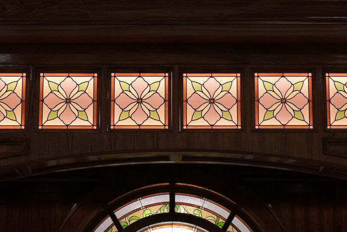 Stained glass panels with floral patterns in pink and yellow, set in a wooden arch. Warm lighting creates a serene ambiance.