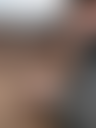 Person in a dark jacket holds a thermometer against a brown horse's side, checking temperature. Clear sky and grassy background.