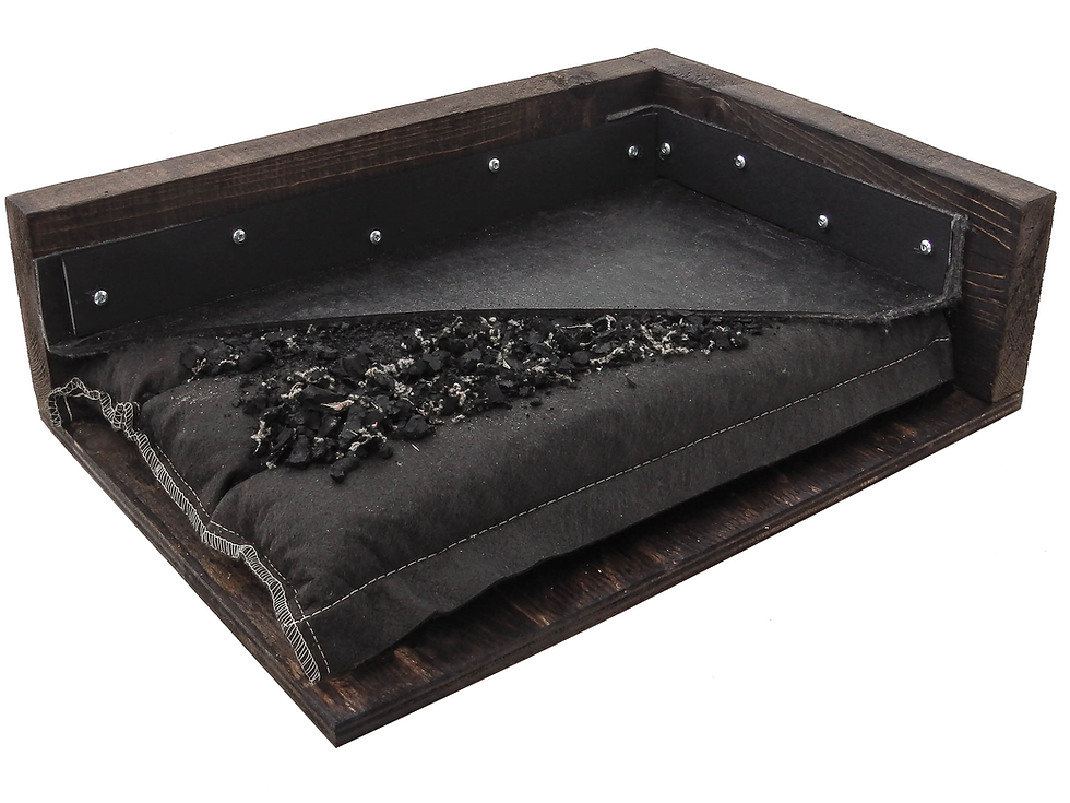 Wooden trap target box with black padding, filled with black debris showing stall mattress components. Stitching visible, surrounded by dark wood panels and screws.