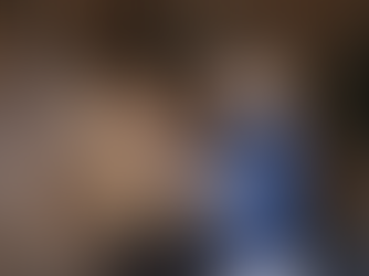 Vet in a blue shirt uses a stethoscope on a brown horse in a stable. Wooden walls and green stall doors are visible in the background.