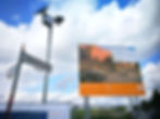 Zeitraffer-Kamerasystem mit Solarmodul neben Bauschild für Schulneubau.