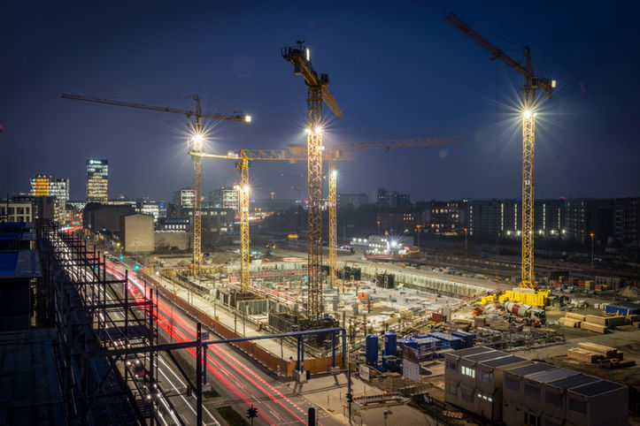 Weitwinkel-Nachtaufnahme der Baustelle "Quartier Heidestrasse" mit hell leuchtenden Flutlichtmasten und Kränen gegen den dunklen Himmel.