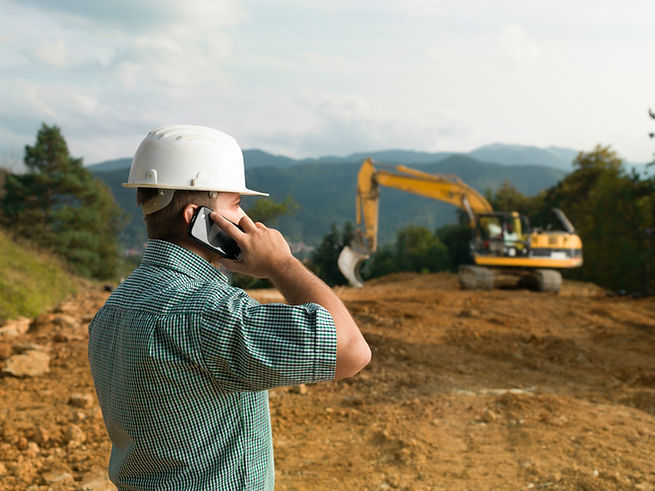 Kontakt zu Contempo Zeitraffer: Bauleiter mit Helm telefoniert auf Baustelle, Bagger im Hintergrund