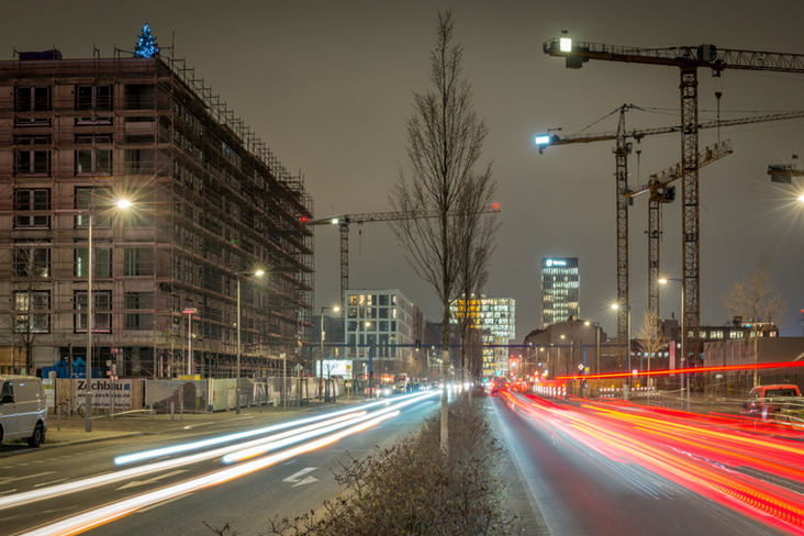 Langzeitbelichtung einer Baustelle mit Lichtspuren des fließenden Verkehrs im Vordergrund.