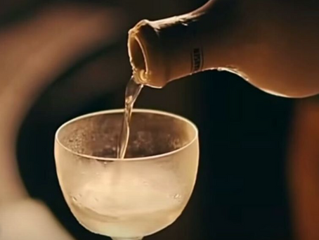 A close-up, warm-toned shot of a clear cocktail being elegantly poured from a dark bottle into a chilled, frosted coupe glass at Muro, Bengaluru.
