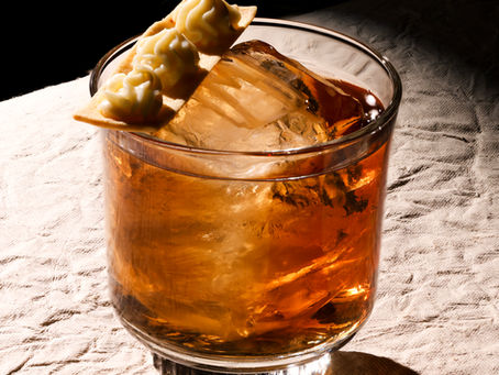 A close-up shot of the Sweet Chin Music cocktail at Muro, showing a crisp lavash garnish topped with three swirls of coconut mousse resting on a large ice cube in a rocks glass.