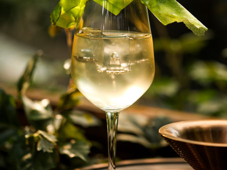 A close-up shot of the Shades Off Green cocktail at Muro, served in a wine glass with a large clear ice cube and an elegant green leaf garnish topped with a small purple flower.