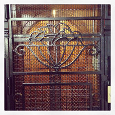 Grille en fer forgé avec motif floral devant un ascenseur.