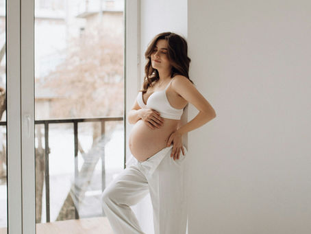 A pregnant woman peacefully leaning on a wall in her home