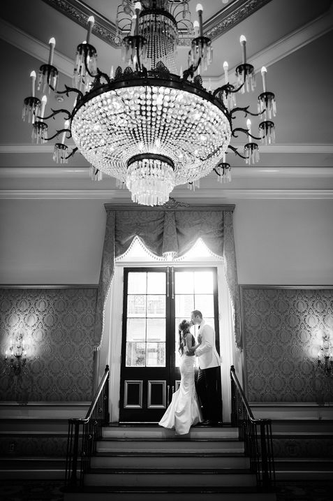 a couple stands at the top of a staircase in front of a door as they embrace on the day of their wedding - Julia Bailey
