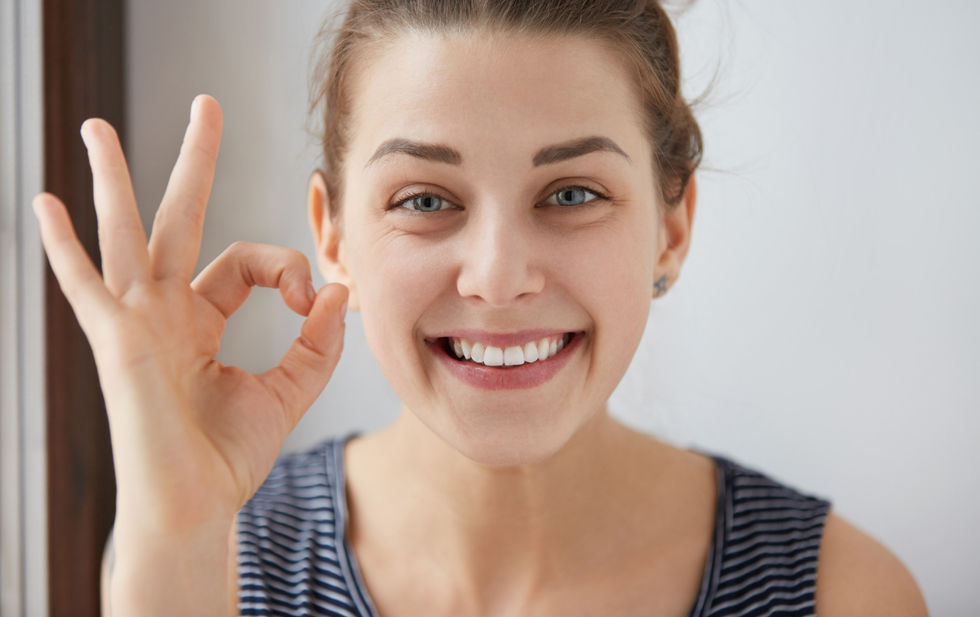 young-european-brunette-female-showing-ok-gesture-with-her-fingers-happy-woman-striped-top