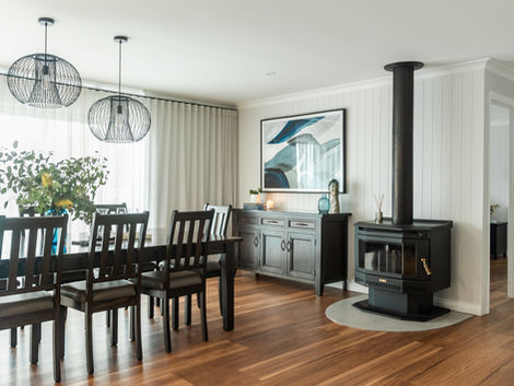 A solidly built home from steel, although the exterior bones were sound, the interior required major upheaval to bring it to life.
With a clear vision of renovating the Kitchen and wet areas, the overall layout needed to be reconfigured. By relocating the lounge where the dining table was and re-positioning the meals area in line with the Kitchen created continuity and flow to an open plan room.
The old laminate Kitchen was dated and tired with an injection of personality needed. By introducing a monochrome palette, the island bench was nominated as the hero of the space featuring black v-groove vinyl cabinetry and detailed handles. The remaining joinery was elevated in smooth laminate finish complimented by mottled, soft white reconstituted stone.
A herringbone marble splash back in the Kitchen also featured in the Master Ensuite within an extensive double walk-in shower. The layout of this space wasn’t too dissimilar to the original layout, however with the deletion of an exterior window and corner spa-bath, the double vanity and shower space were well catered for. With the addition of tubular skylights, brushed nickel tapware, feature lighting and a light grey lappatto porcelain tile throughout, this room now exudes a tranquil sophistication.
By painting the entire interior in a warm grey hue, installing high-end vinyl planks over existing flooring, adding v-groove paneling to accent walls and installing feature pendant and wall lights instantly elevated the overall palette.
With the addition of soft, s-fold sheers curtains, new furniture and artwork, this home now inherits a sense of welcome for anyone who visits to be entertained in comfort and style.