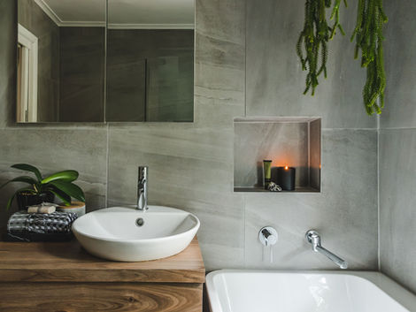 A main bathroom in need of a facelift to cater to needs of a busy family of five.
Walls were stripped bare and a contemporary design was forecast to provide an easy to maintain, tranquil retreat for adults and a user-friendly design for children.
Large format floor and wall tiles laid to the ceiling create a ‘hotel inspired’ look and feel. This slightly darker shade works wonders in the light filled space, inheriting a subtle vein creating interest and texture.
A custom made vanity and tall cupboard specified in a deep feature walnut colour accompanied by an in-wall shaving cabinet assist with maximising on storage and space. Unique round timber handles were installed on each unit to create a sense of style and uniqueness
Walk in shower, simple and sleek bathroom fittings and fixtures along with a back to wall freestanding bath complete the design to suit this growing family for years to come.