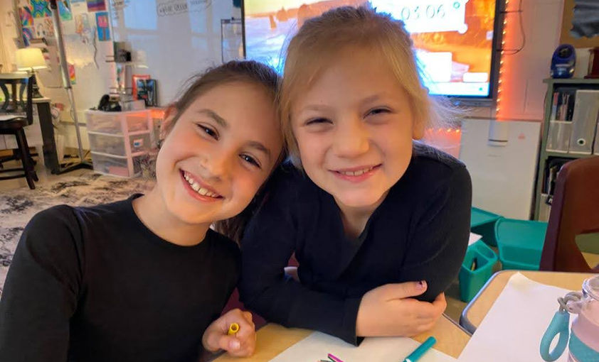 Two girls smiling, drawing 'KIND'