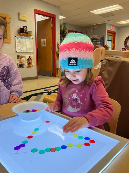 preschool girl making triangle on a light board