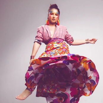 Woman dancing in vibrant floral skirt, pink top, and large earrings.
