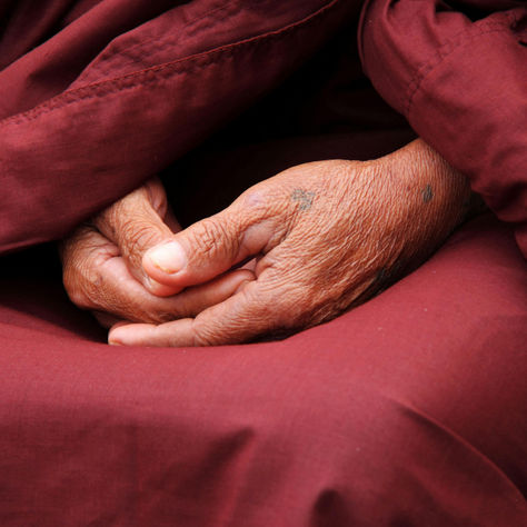 Close up of hands clasped in the lap of a person wearing red monks robs.
