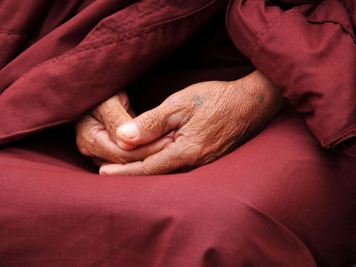 Close up of hands clasped in the lap of a person wearing red monks robs.
