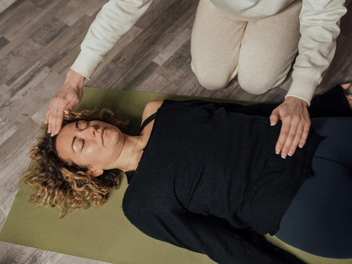 A Woman Meditating while Lying Down with a person's hands positioned above the forhead and stomach