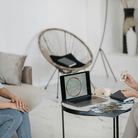 Woman holding tarot card with astrology chart on computer in front of her