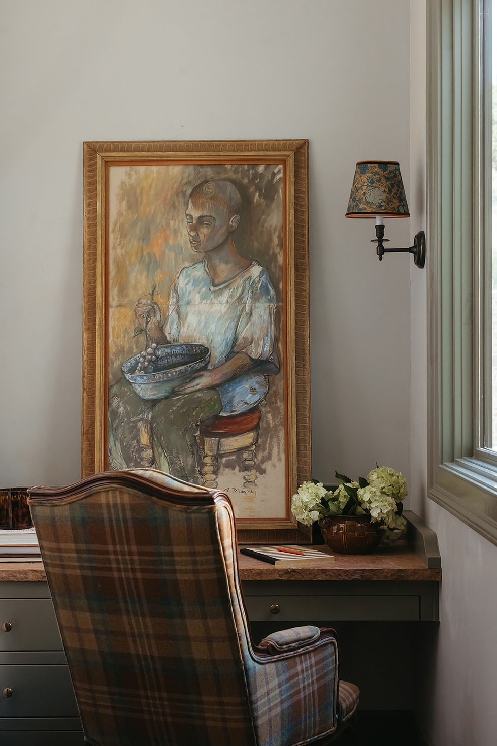 Framed painting of person seated with bowl, wall-mounted lamp.