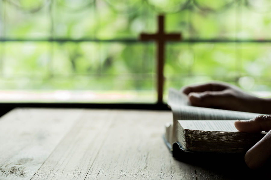 Man reading bible and a cross at the background