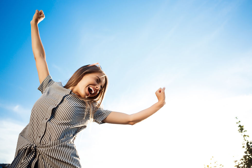 Woman in a striped dress joyfully stretches arms under a clear blue sky, showing excitement and energy.