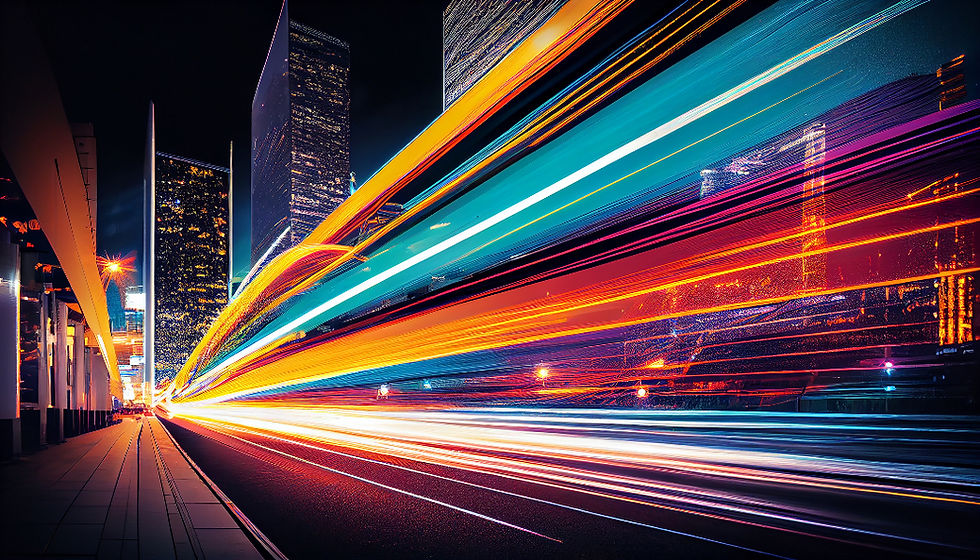 Colorful long-exposure light trails sweep through a nighttime city street beside tall skyscrapers and a sidewalk.